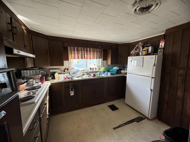 kitchen featuring wooden walls, dark brown cabinets, and white appliances