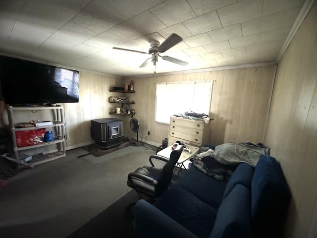 carpeted living room featuring ceiling fan, wood walls, a wood stove, and ornamental molding