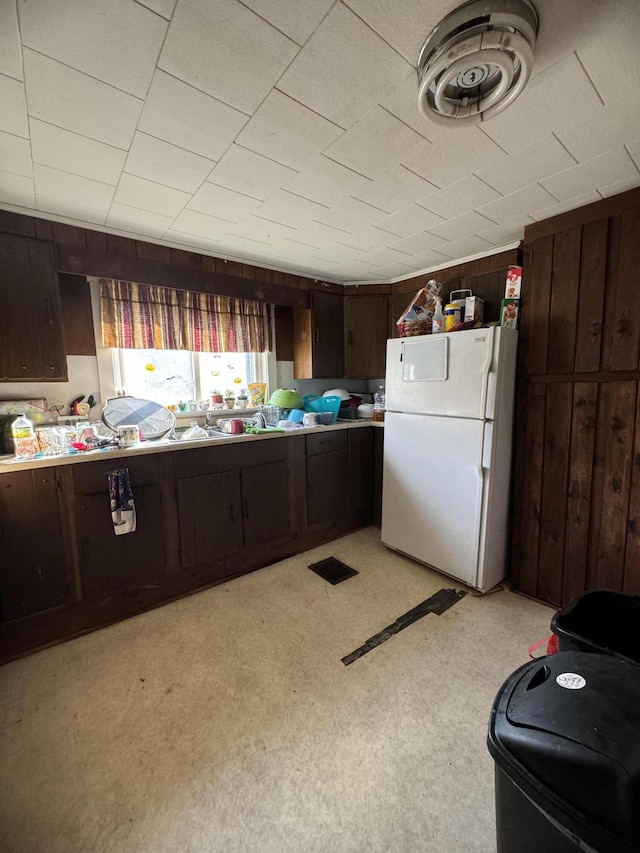 kitchen featuring white fridge, dark brown cabinetry, wooden walls, and light colored carpet