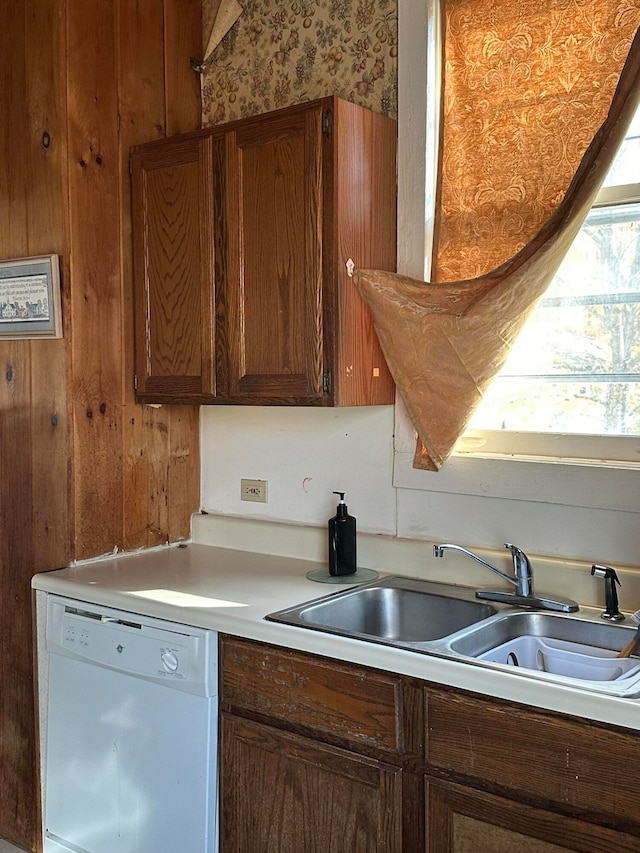 kitchen with white dishwasher, sink, and wooden walls