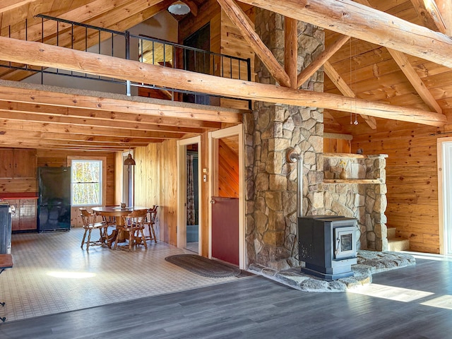 unfurnished living room with wooden ceiling, a wood stove, hardwood / wood-style floors, wood walls, and high vaulted ceiling