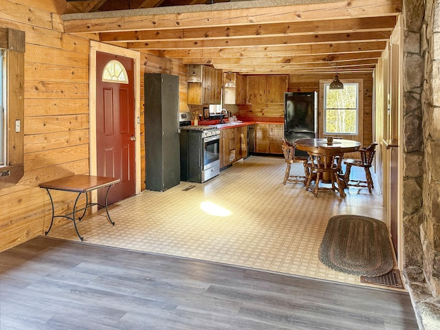 kitchen featuring light hardwood / wood-style flooring, wooden walls, black refrigerator, stainless steel range with gas stovetop, and sink