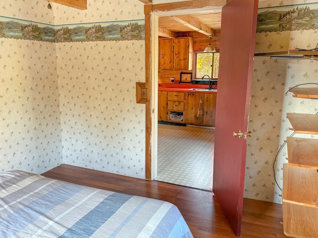 unfurnished bedroom featuring sink, beamed ceiling, and hardwood / wood-style flooring