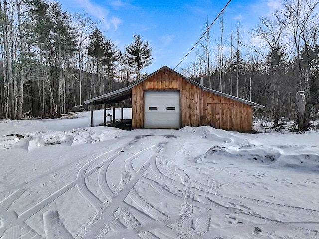 snow covered property with a carport, a garage, and an outdoor structure