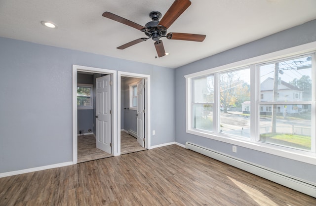 unfurnished bedroom featuring ceiling fan, hardwood / wood-style flooring, a baseboard radiator, and ensuite bath