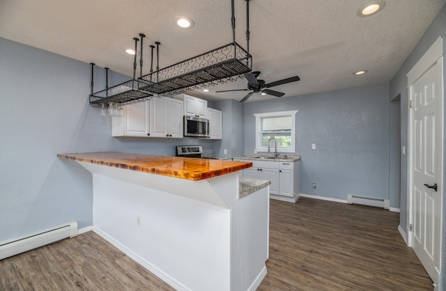 kitchen featuring a baseboard radiator, wood counters, kitchen peninsula, stainless steel appliances, and white cabinets