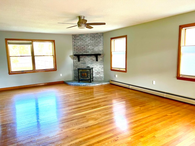 unfurnished living room with a baseboard radiator, a textured ceiling, a wood stove, ceiling fan, and light hardwood / wood-style flooring