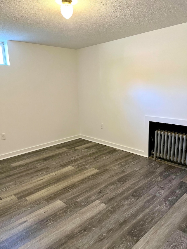 empty room with dark wood-type flooring, a textured ceiling, and radiator