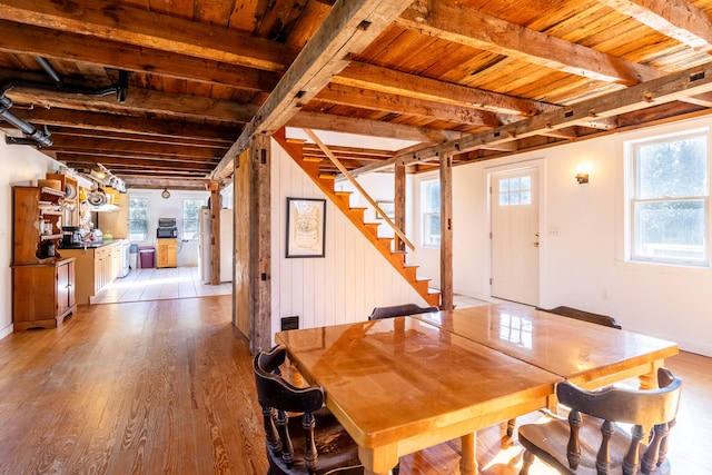 dining room featuring wood walls, wooden ceiling, beamed ceiling, and light wood-type flooring