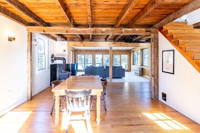 dining area with light hardwood / wood-style floors, wood ceiling, beamed ceiling, and a wood stove