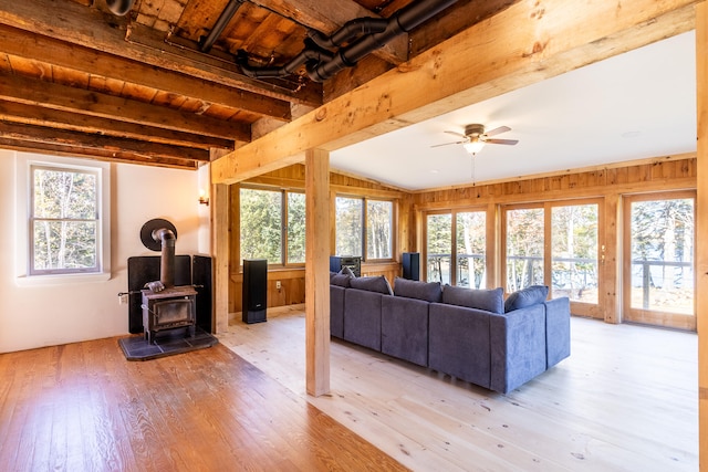 living room with wood walls, lofted ceiling with beams, a wood stove, ceiling fan, and light hardwood / wood-style flooring