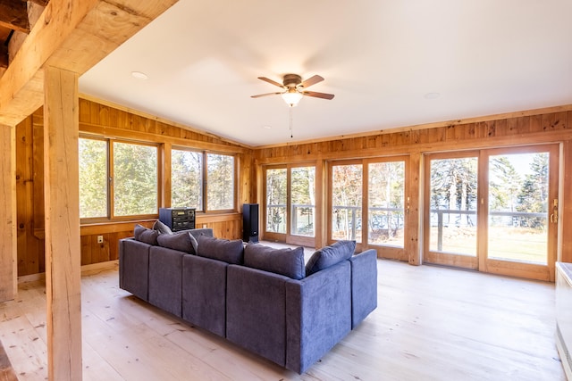 living room with light hardwood / wood-style floors, lofted ceiling, wooden walls, and ceiling fan