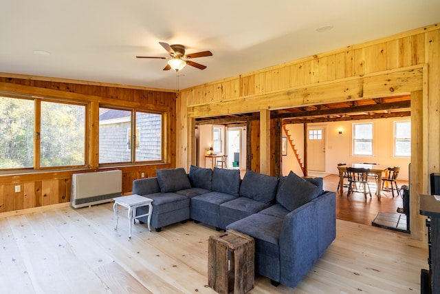 living room with wooden walls, heating unit, light wood-type flooring, and ceiling fan