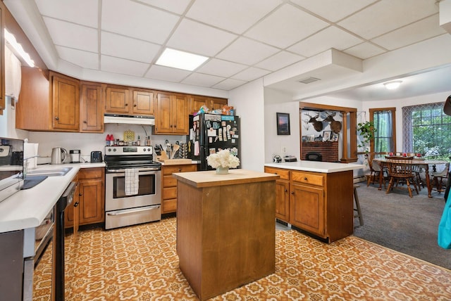 kitchen featuring a kitchen island, a breakfast bar, a paneled ceiling, black appliances, and light colored carpet