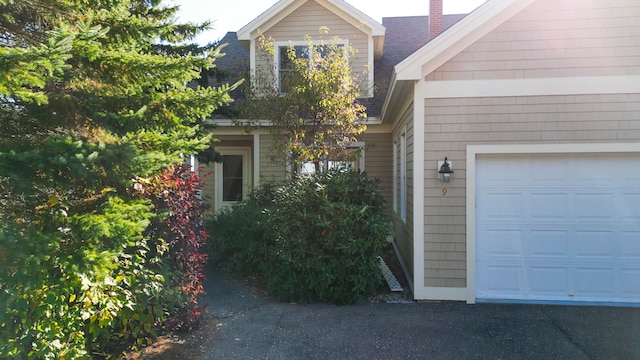 exterior space with a garage, a shingled roof, and a chimney