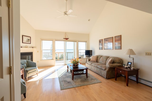 living room with a ceiling fan, high vaulted ceiling, a glass covered fireplace, and light wood-style flooring