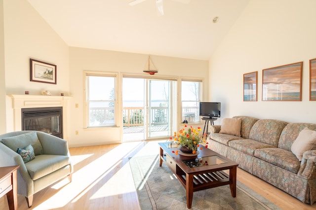 living room featuring a ceiling fan, high vaulted ceiling, a glass covered fireplace, and wood finished floors