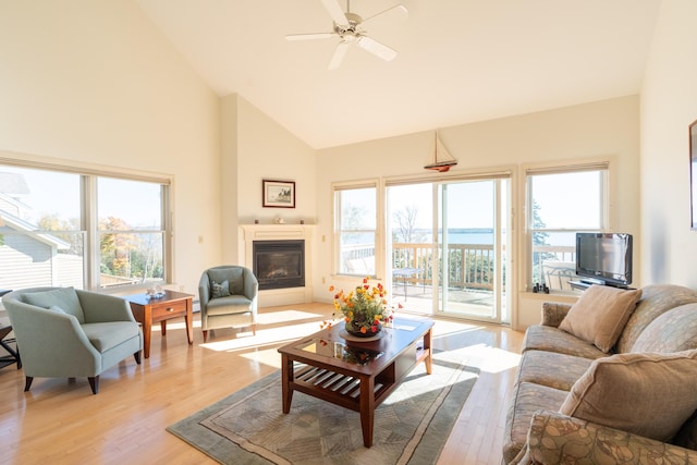 living room featuring a glass covered fireplace, high vaulted ceiling, a ceiling fan, and light wood finished floors