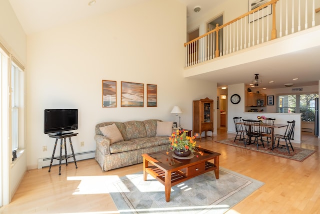 living room featuring a high ceiling, baseboard heating, and wood finished floors