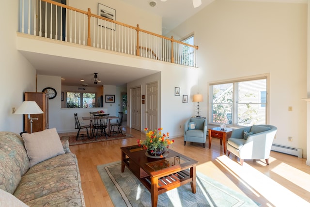 living area featuring a high ceiling, a baseboard heating unit, and wood finished floors