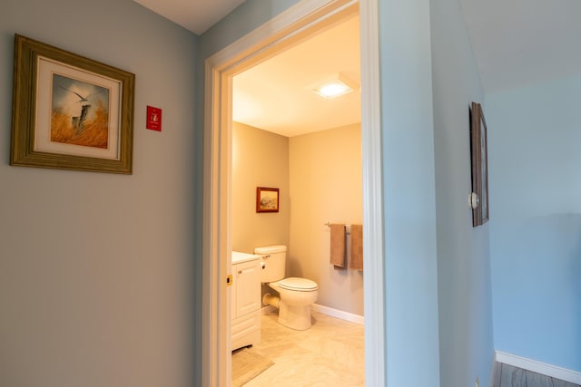 half bathroom with toilet, baseboards, and vanity