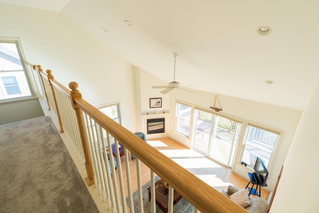 corridor featuring high vaulted ceiling, light colored carpet, and an upstairs landing