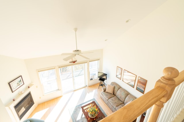 living room featuring ceiling fan, a glass covered fireplace, lofted ceiling, and light wood finished floors