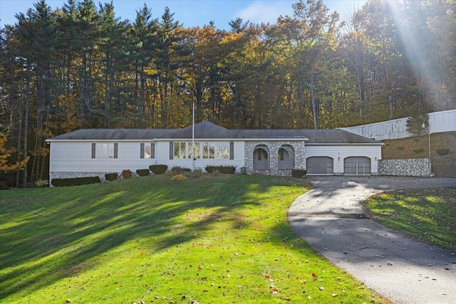 view of front of house featuring stone siding, aphalt driveway, a front yard, and a garage