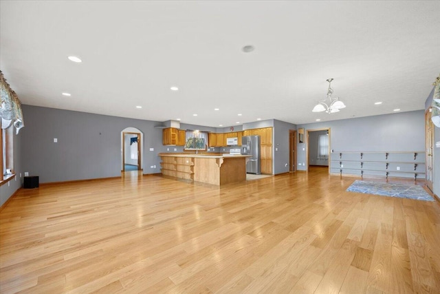 unfurnished living room with light wood finished floors, arched walkways, a chandelier, recessed lighting, and baseboards