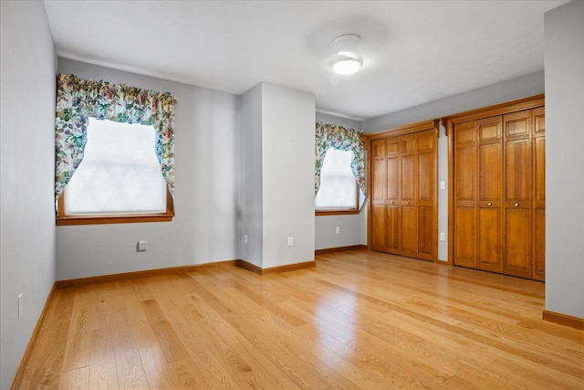 unfurnished bedroom featuring baseboards, light wood-style flooring, and multiple closets