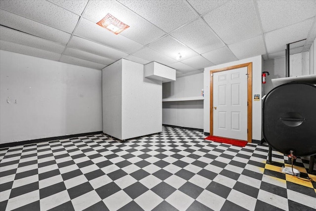 finished basement featuring baseboards, a drop ceiling, heating fuel, and light floors