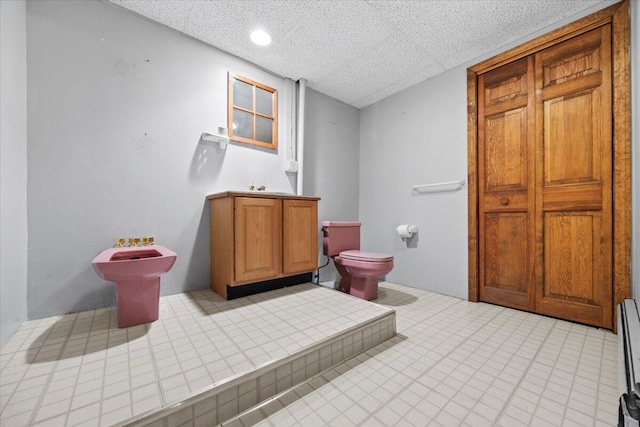 bathroom featuring baseboard heating, toilet, and a sink