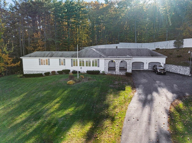view of front facade with a front lawn, stone siding, a garage, aphalt driveway, and a view of trees