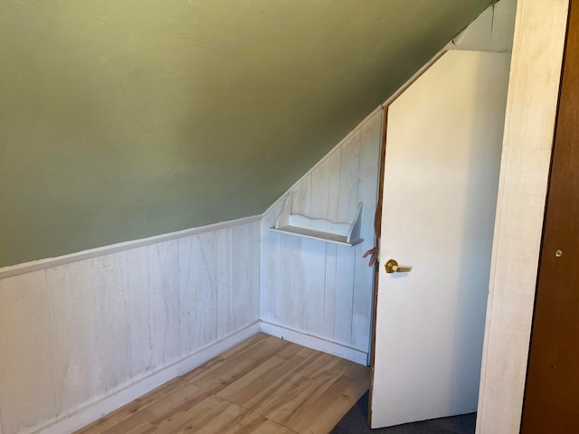 additional living space featuring lofted ceiling, wood walls, and light wood-type flooring