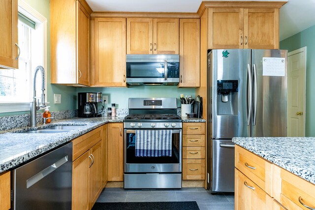 kitchen with sink, light stone counters, stainless steel appliances, and dark tile patterned flooring