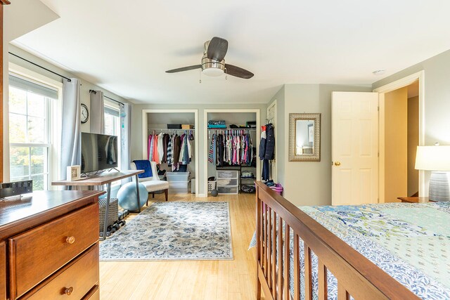 bedroom with ceiling fan, light hardwood / wood-style flooring, and two closets