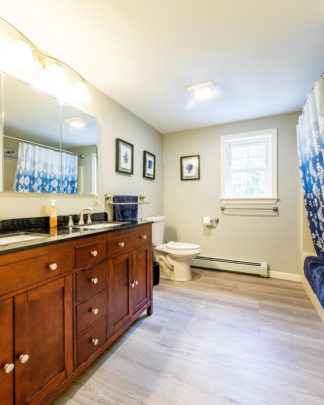 bathroom with a shower with shower curtain, toilet, baseboard heating, vanity, and hardwood / wood-style flooring