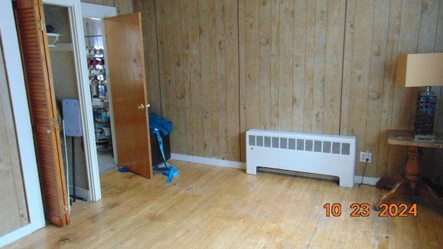 bedroom featuring radiator, a closet, light hardwood / wood-style flooring, and wooden walls