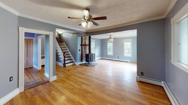 spare room with a wood stove, a textured ceiling, a baseboard radiator, and light wood-type flooring