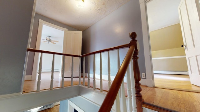 staircase with lofted ceiling, a baseboard heating unit, wood-type flooring, and ceiling fan