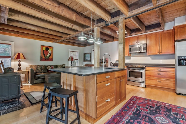 kitchen with appliances with stainless steel finishes, sink, wooden ceiling, beam ceiling, and a kitchen island with sink