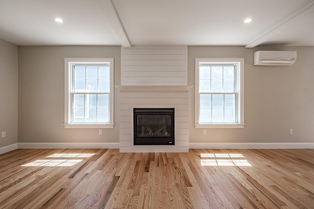 unfurnished living room with a wall unit AC, wood finished floors, and plenty of natural light