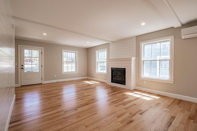 unfurnished living room featuring light wood-style floors, an AC wall unit, a large fireplace, recessed lighting, and baseboards