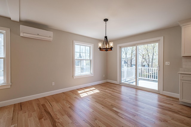 unfurnished dining area featuring baseboards, an AC wall unit, light wood finished floors, and a chandelier