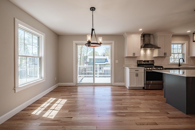 kitchen with wall chimney range hood, light countertops, white cabinetry, baseboards, and gas range