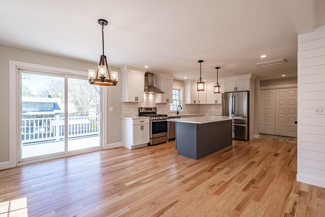 kitchen with light countertops, wall chimney exhaust hood, light wood finished floors, and stainless steel appliances