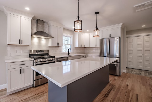 kitchen featuring wall chimney range hood, light wood-type flooring, light countertops, a sink, and appliances with stainless steel finishes