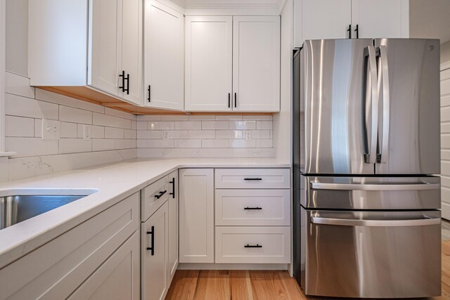 kitchen with white cabinets, freestanding refrigerator, backsplash, and light wood-style flooring