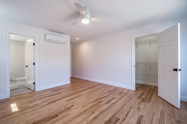 unfurnished bedroom with a walk in closet, baseboards, a closet, an AC wall unit, and light wood finished floors