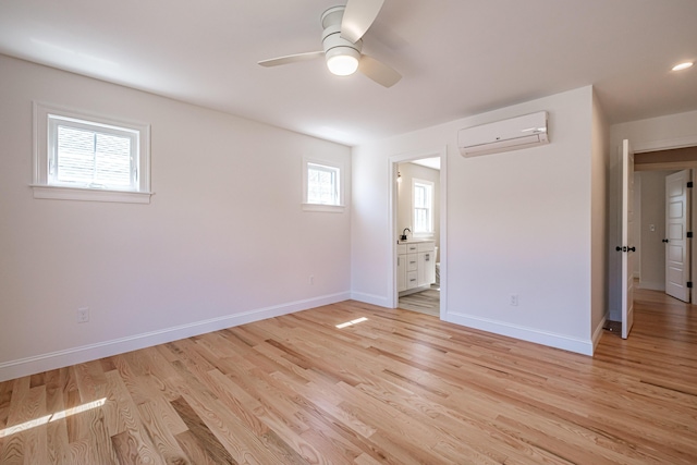 spare room featuring an AC wall unit, a ceiling fan, baseboards, and light wood-type flooring